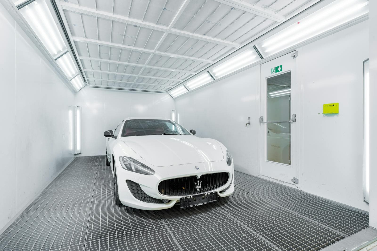 White coupe parked inside a bright automotive spray booth.