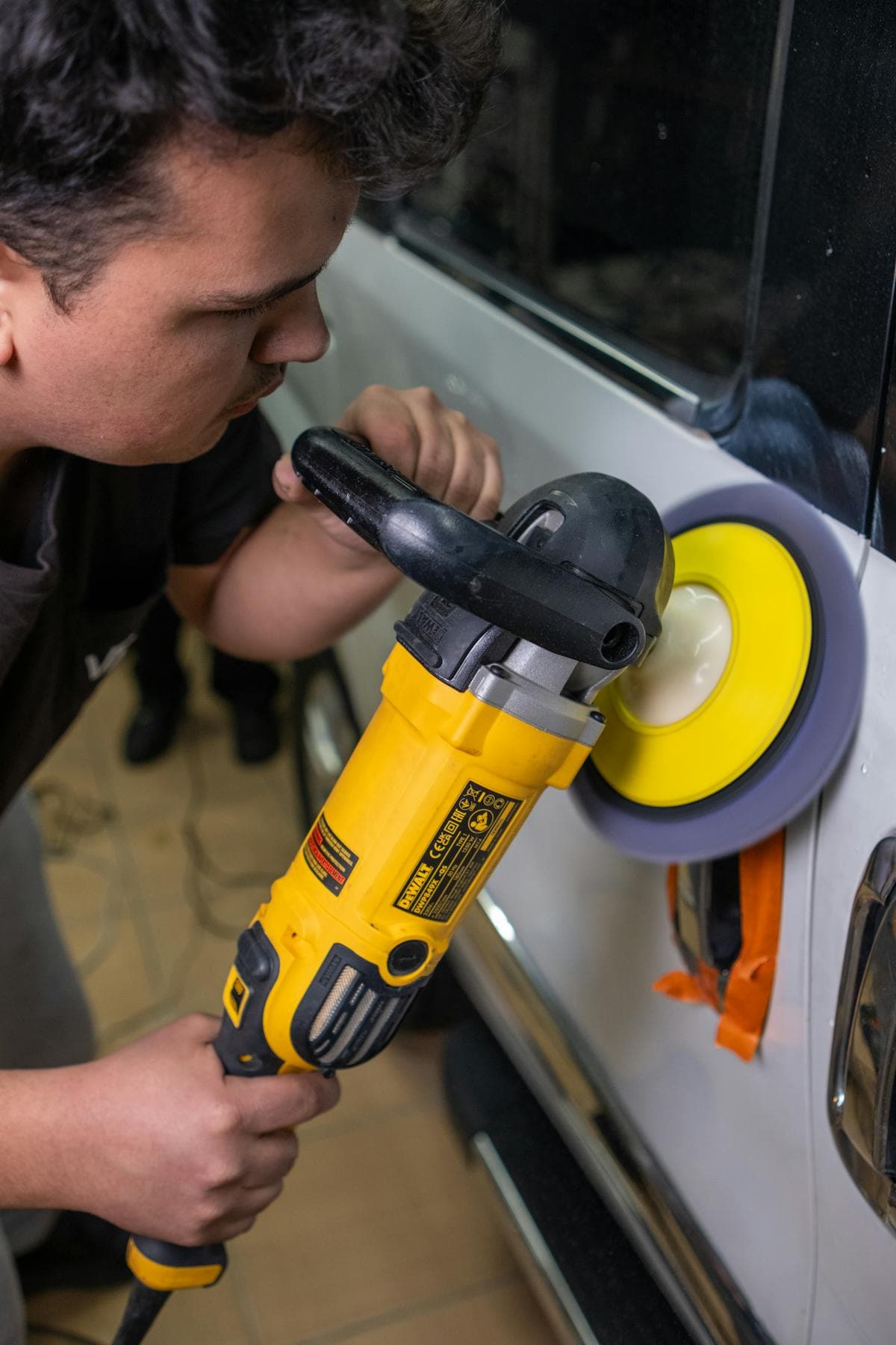 Technician polishing a dark vehicle panel during paint correction.